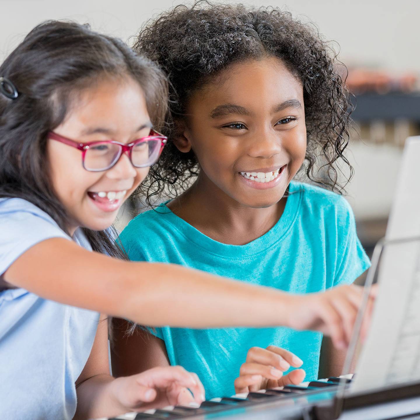 two children sitting at a piano reading sheet music